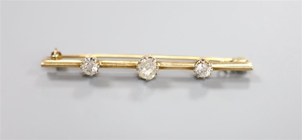 A yellow metal and three stone diamond set bar brooch, 58mm, gross 4.9 grams, set with one oval cushion and two round cut stones.